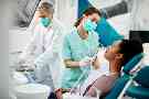 Gothaer Ratgeber Gesunde Zähne: Frau liegt beim Zahnarzt auf einem Behandlungsstuhl. Ihre Zähne werden von einem Zahnarzt und einer Zahnarzthelferin behandelt.
